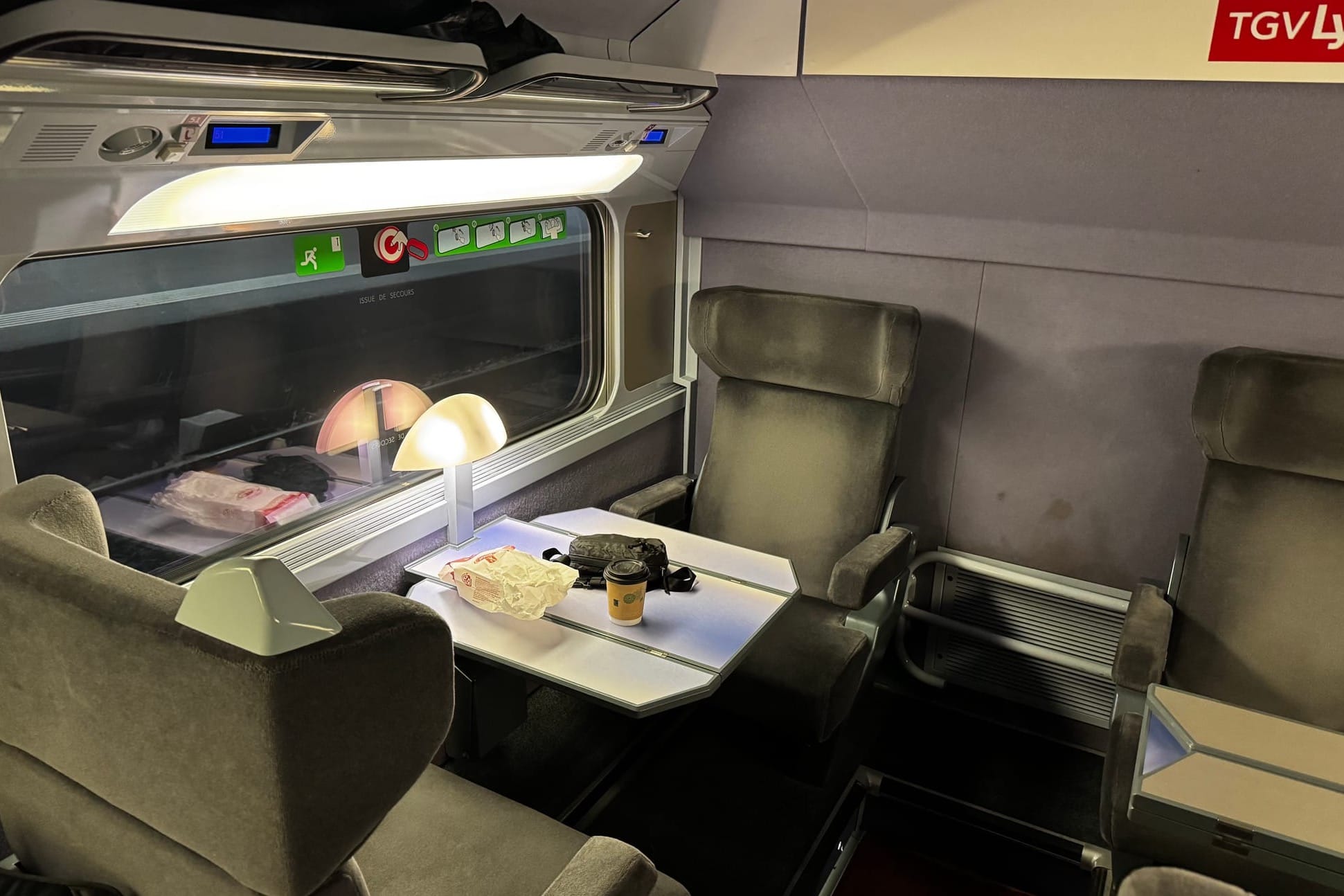 Zwei Sitze im TGV. Auf dem Tisch hat es verschiedene Gegenstände, inklusive einem Kaffeebecher.